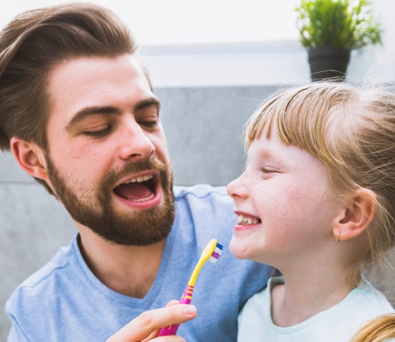 A father helping his child brush his teeth